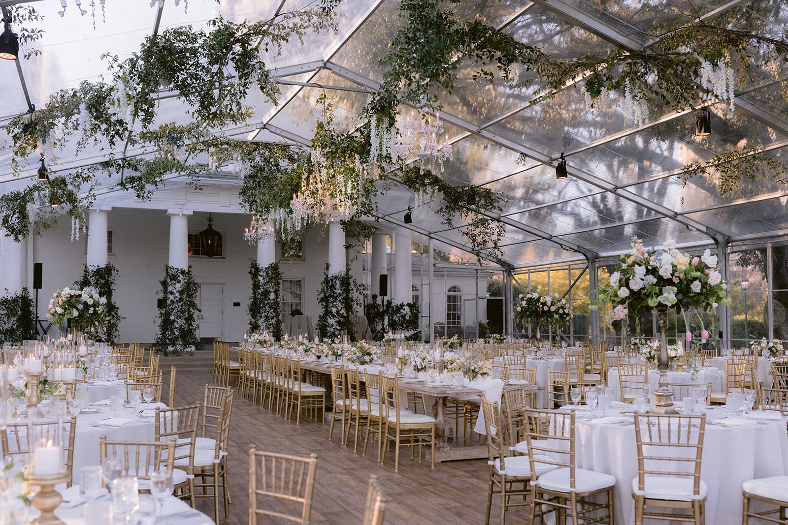 Glass-tented reception with a lush greenery ceiling installation and long banquet tables