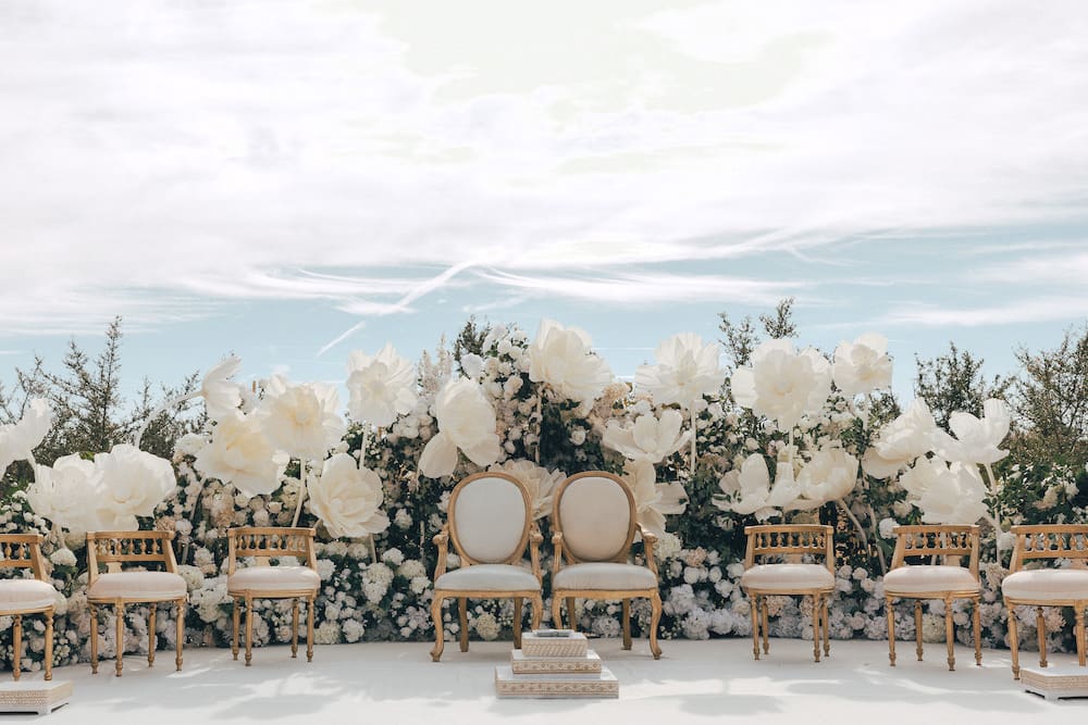 Open-air wedding ceremony with a lined aisle and ghost chairs beneath a bright sky