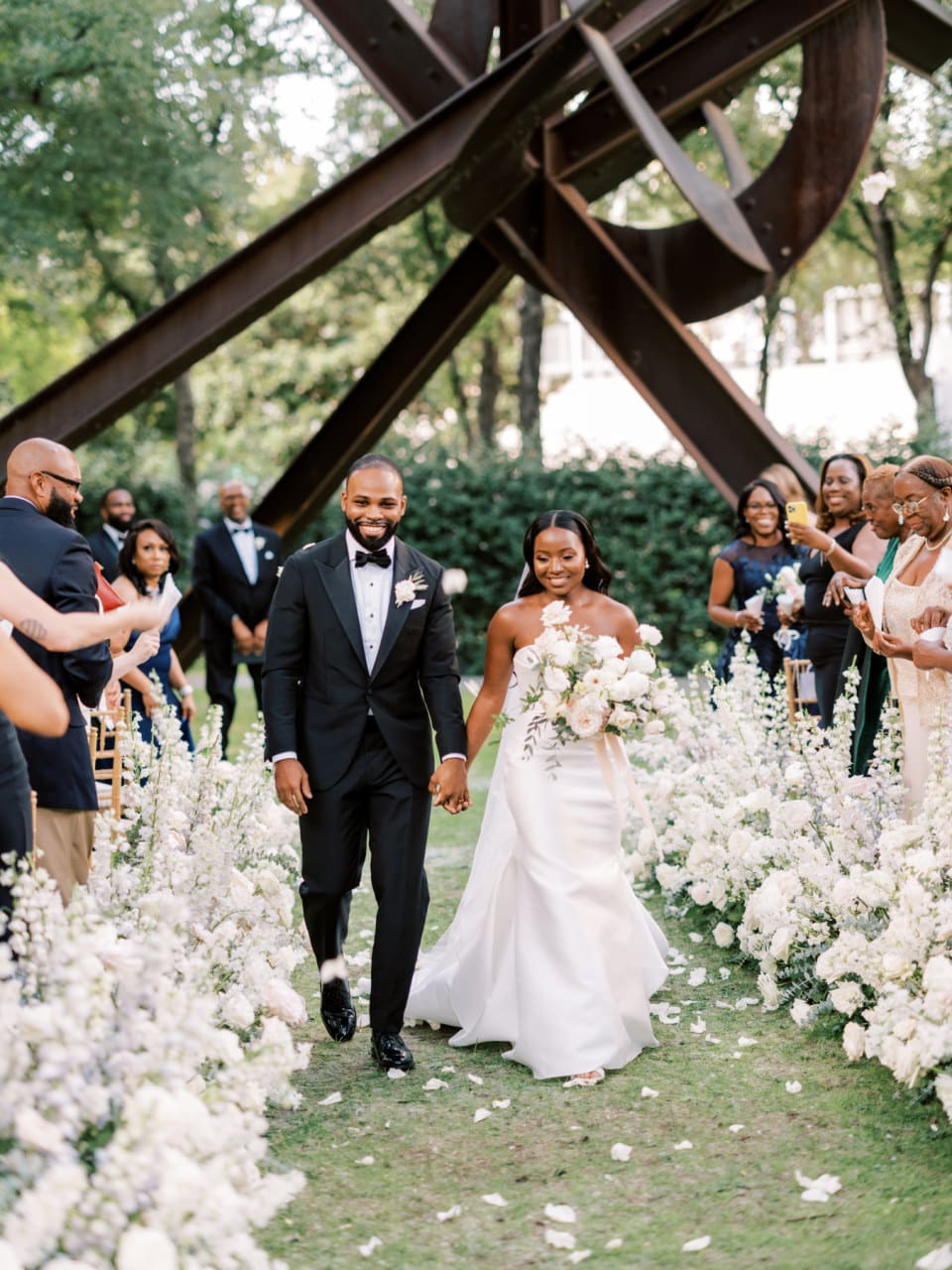Newlyweds' joyful recessional down a lined garden aisle surrounded by guests