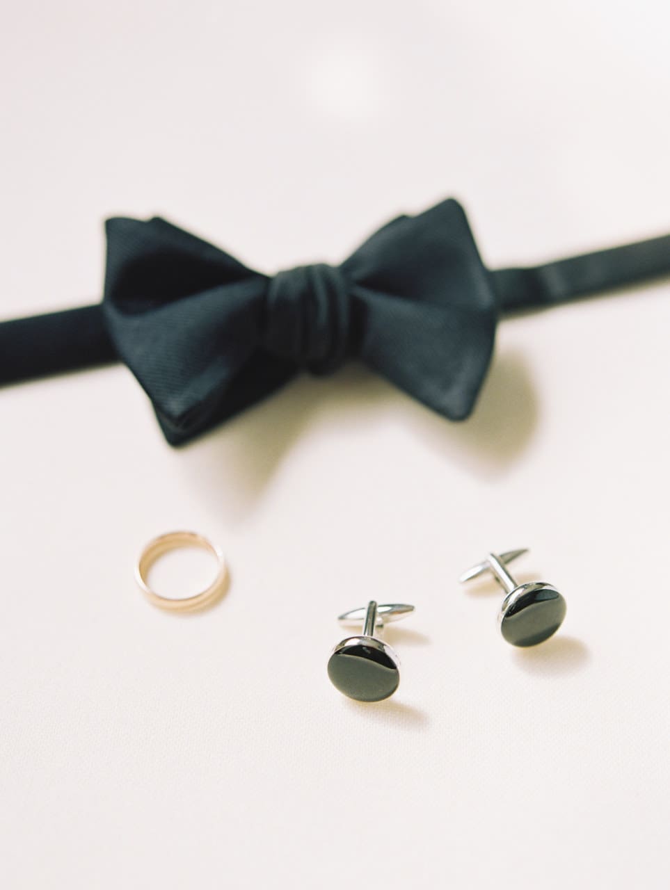 Groom's wedding-day details styled flat lay — bow tie, cufflinks and band